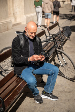 Mature man using smartphone while sitting on a bench next to a bicycle