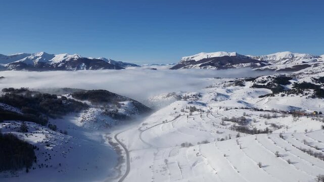 Drone Aerial View of Snow Covered Mountain Peaks with Fog Filled Valley in Winter Landscape