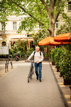 Mature man walking with bicycle in city square in a european street