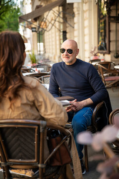 Mature man and woman sitting at outdoor cafe terrace, talking and smiling