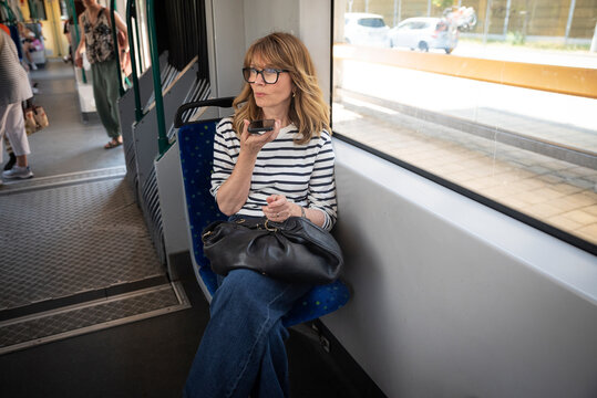 A middle-aged woman riding the tram and using a smarpthone