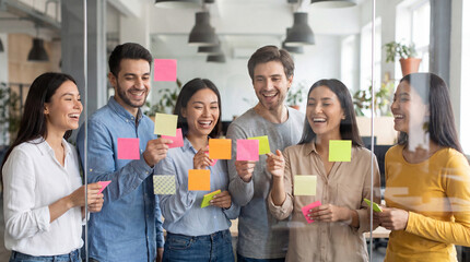 Fototapeta premium Group of diverse young professionals collaborating with sticky notes on glass wall in modern office space during brainstorming session
