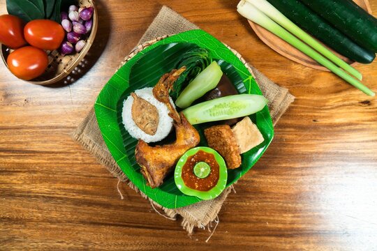 Authentic Indonesian Cuisine: A vibrant plate of traditional Indonesian fare featuring crispy fried chicken, rice, cucumber slices, tofu, and a flavorful sambal, presented on a banana leaf.