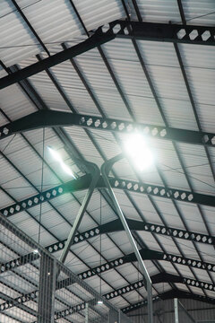 Industrial Warehouse Ceiling Structure: A detailed view of the steel framework and corrugated metal ceiling inside an industrial warehouse, illuminated by bright overhead lights.