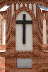 Fototapeta premium Wooden cross on a red brick gothic church wall with memorial plaque