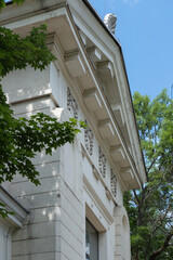Classic building facade wall with ornate cornice stands near green trees © dimetradim