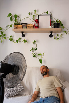 Hispanic man feeling exhausted despite fan during extreme summer heat