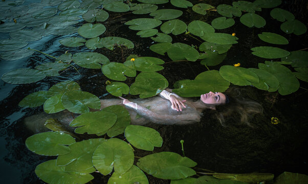 Mystical Slavic water nymph or Mavka floating in a dark river among water lilies, ancient mythology concept with a beautiful woman as a river spirit, pagan folklore and ethno fantasy atmosphere