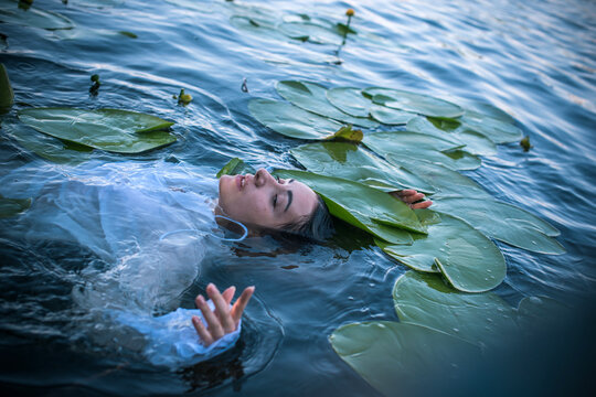 Mystical Slavic water nymph or Mavka floating in a dark river among water lilies, ancient mythology concept with a beautiful woman as a river spirit, pagan folklore and ethno fantasy atmosphere