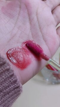 Applying pinkish red lip tint to palm skin using makeup brush applicator. Close up view. Lip color product swatch for beauty presentation.