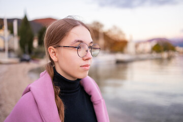 Side profile portrait of a teenage girl in glasses by the calm sea at sunset. © Lena May