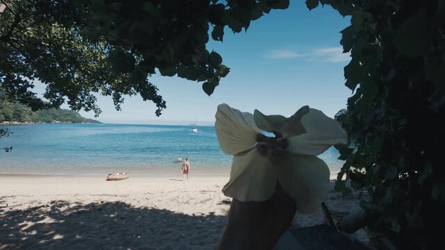 Person rotates flower in the head with sandy sunny beach on the background