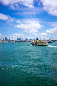 A classic Istanbul ferry steams across the wide turquoise Bosphorus with the city's densely developed shoreline stretching across the horizon.
