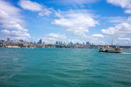 A classic Istanbul ferry sails past the historic European waterfront skyline on the sparkling turquoise Bosphorus on a sunny day.
