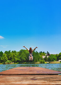 A shot of an attractive young woman in a bikini at a small lake. She is jumping into the water from a wooden jetty. "Jumping into vacation" concept.