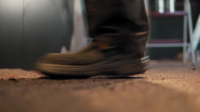 Work boots walking on dust covered floor inside art workshop.