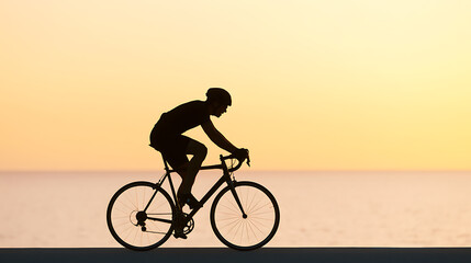Fototapeta premium Silhouette of a male cyclist riding a road bike against a stunning golden sunset over calm ocean water, conveying peace and endurance