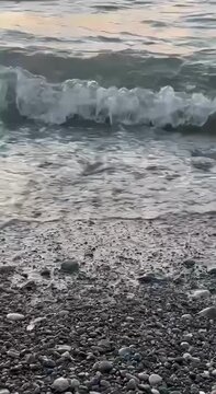 Gentle ocean wave reaching rocky shoreline with natural coastal texture at peaceful seaside beach