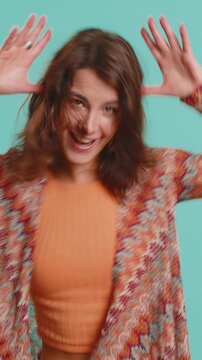 Funny comical playful young woman making silly facial expressions and grimacing, fooling around, showing tongue, idiotic expression. Lady isolated alone on blue studio background. People lifestyles