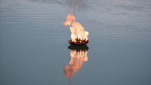 A flaming bowl floats on tranquil water, its reflection mirroring the fire
