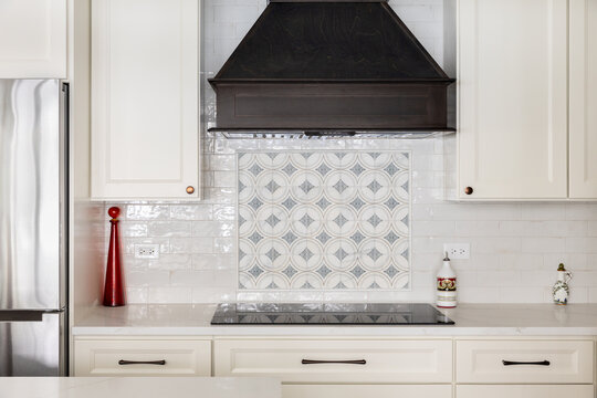 A kitchen range hood detail with a dark wood range hood, cream cabinets and marble countertop, and a white subway and pattern tile backsplash.