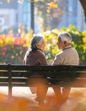 Elderly couple sitting on a park bench in autumn sunlight.
