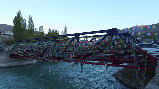 Leh Ladakh Kullu Manali Himachal Pradesh India. Buddhist prayer flags fluttering in the wind. Old Iron bridge over Beas river flowing through beautiful snow covered Indian mountain in Himalayas.	