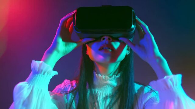A young woman with her eyes covered by a VR headset, wearing a white shirt and black pants, surrounded by colorful lights that suggest an immersive environment.