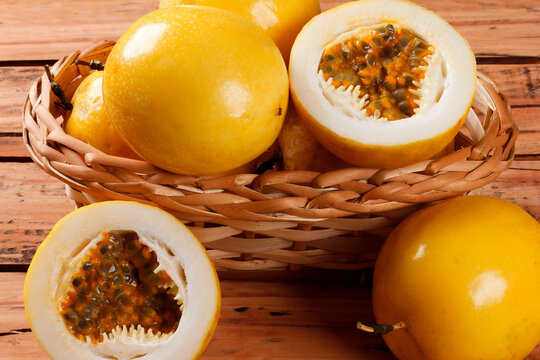 Whole and cut yellow passion fruit showing fresh pulp and seeds in a rustic basket on a wooden table.