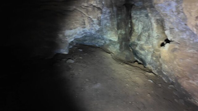 Interior of a low vaulted limestone cave illuminated from the lower left by a handheld light, revealing a central stepped rock ledge extending toward the mid right, rough
