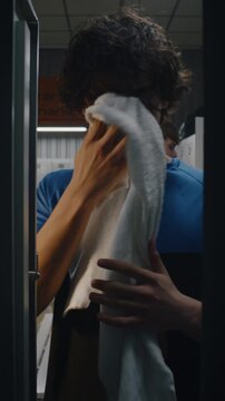 Teenage Opening Locker After Game. Sweaty Young Man Wipes Wet Face, Pulls Out Smartphone to Check Notifications or Messages, and Then Closes Metal Door. Modern Youth, Digital Lifestyle. Vertical Shot.