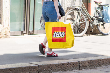 Obraz premium Street photo. Carrying Large Yellow LEGO Shopping Bag. Shopping, Adidas sneakers, Wear comfortable shoes. Milan, Italy - June 24, 2026