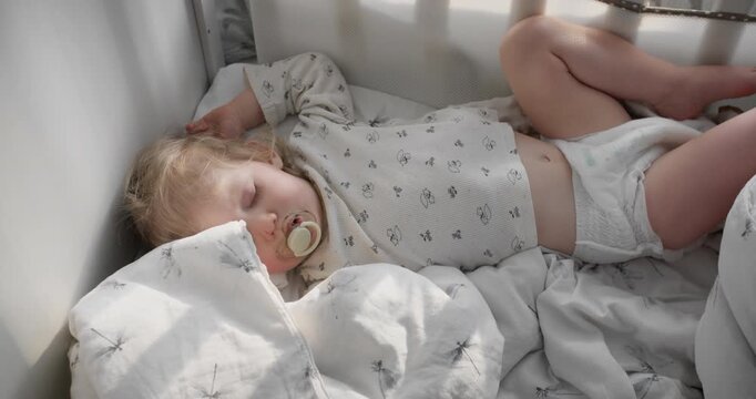 Blonde toddler sleeps soundly with pacifier in white crib soft natural light. Parenting blogs, baby product ads, childhood development, and family lifestyle content