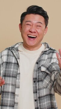 Asian middle-aged man pointing finger to camera, laughing out loud, taunting making fun of ridiculous appearance, funny joke anecdote, bullying, abuse. Adult Chinese guy isolated on beige background