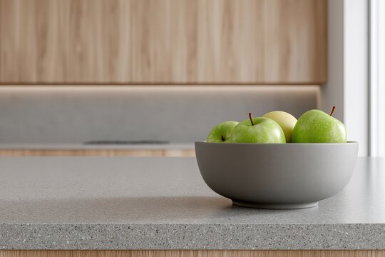 A modern kitchen counter with a bowl of fresh green apples and minimalist wooden cabinetry in the background.