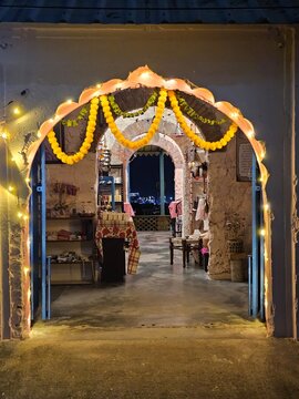 A beautifully decorated archway adorned with marigold garlands and fairy lights leads into a cozy indoor setting, evoking warmth and celebration during the festive season.
