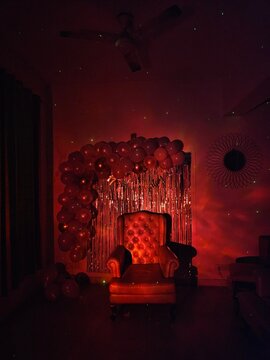 A cozy, illuminated armchair is positioned in a dimly lit room adorned with shimmering balloons, creating a festive and intimate atmosphere perfect for celebrations.