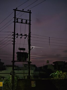 A serene night scene in Delhi featuring a power pole and overhead wires, illuminated by a solitary streetlight, casting a calm ambiance under the twilight sky.