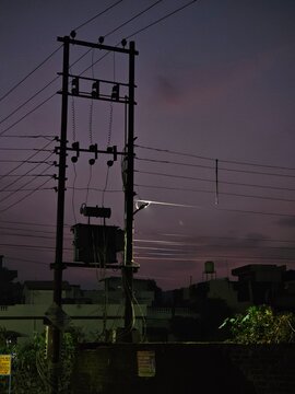 In a dimly lit urban setting, a power pole stands against the twilight sky, highlighting the intricate web of electrical wires and casting a mysterious atmosphere.