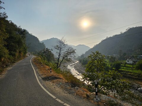 A serene landscape featuring a winding road beside a river, surrounded by hills and trees, with a soft sunset creating a peaceful atmosphere.