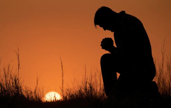 Silhouette of a person kneeling at sunrise with hands clasped