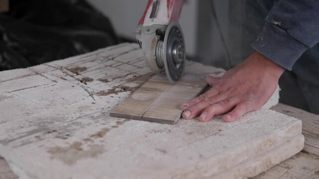 Close workshop view shows hand guiding circular saw through narrow wood plank on worn stone work surface, with cropped worker arm in blue sleeve, dusty textures, muted tones, and