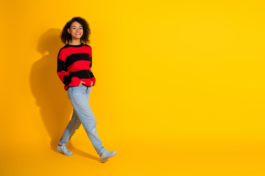 Young woman in a red and black striped sweater walking against a bright yellow studio background