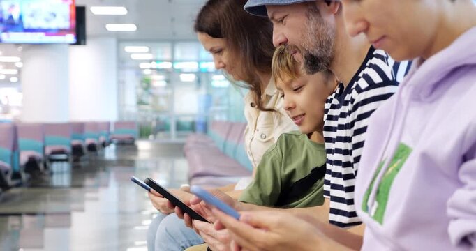 Mother, father and son are sitting in the waiting room of an airport terminal and are using their smartphones, maybe watching travel photographs. Selective focus on young boy.