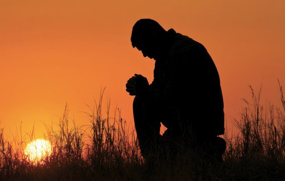 Silhouette of a man praying at sunset amidst tall grass