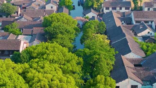 Aerial bird's-eye panorama of Zhouzhuang Ancient Town, classic Jiangnan water town with stone arch bridges, ancient Chinese waterside buildings, canals and lush green trees
