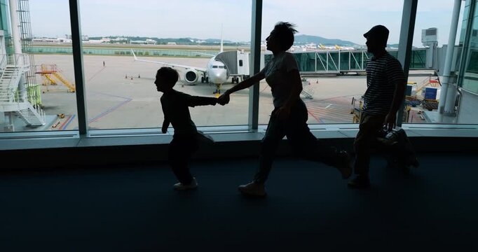 Family silhouettes rushing through airport terminal, holding hands, embodying shared concern about missing their flight, likely due to a mistake with time or gate. Slow motion shot