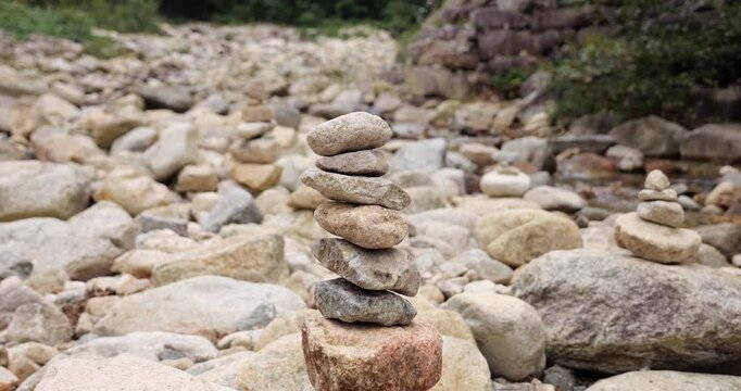 Young woman carefully balancing smooth stones in rather dry riverbed, put one more at top, creating delicate tower with patient concentration and cautious hand movements
