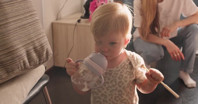 Child taking first unsupported steps indoors while holding everyday items. Early motor skill development and growing mobility