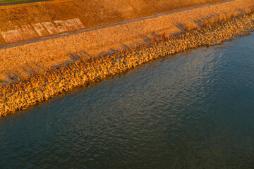 Obraz premium Golden hour riverside with a rocky embankment, calm water and warm tones on stones, tranquil landscape and soft reflections